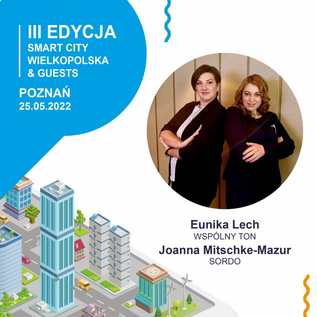 Dwóch tłumaczy ustawionych do siebie bokiem, patrzących w naszą stronę na tle plakatu Smart City